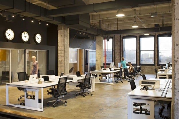 Interior photo of a modern, open concept office space with four people to a desk and laptops.