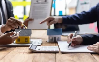 Real estate agent calculates property value with customer, discussing investment potential surrounded by paperwork. Consultation on buying, selling, or renting.